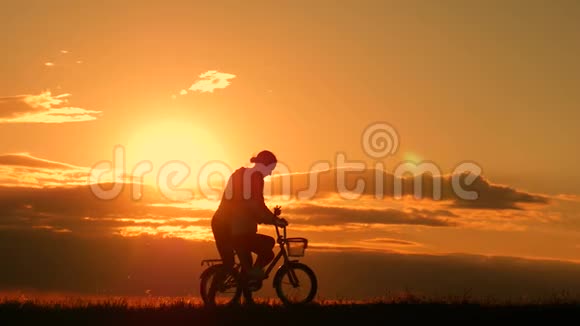剪影自行车可爱的家庭在草地上日落时间母亲和婴儿在日落时骑自行车的剪影生活方式视频的预览图