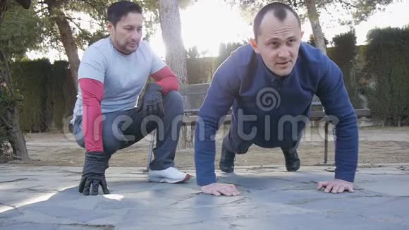 与户外私人教练一起健身健身男子在公园做超级慢俯卧撑作为锻炼的一部分视频的预览图