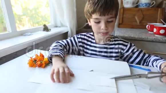 专心致志的5岁男孩用剪刀热情地剪纸伸出舌头视频的预览图