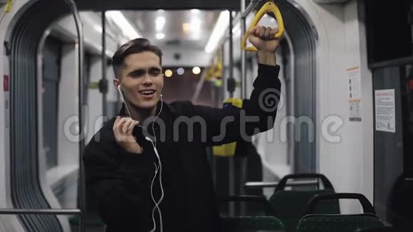 戴耳机听音乐和乘坐公共交通工具跳舞的帅哥的肖像他握着扶手视频的预览图
