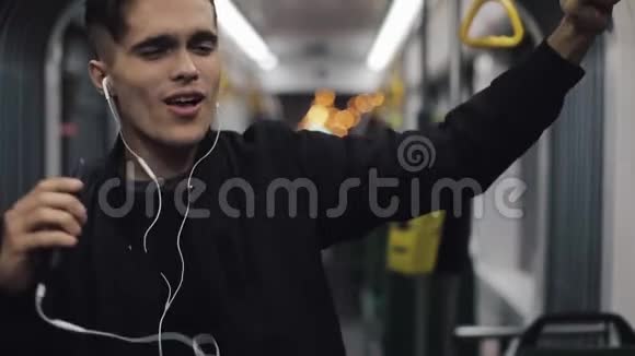 戴耳机听音乐和乘坐公共交通工具跳舞的帅哥的肖像他握着扶手视频的预览图