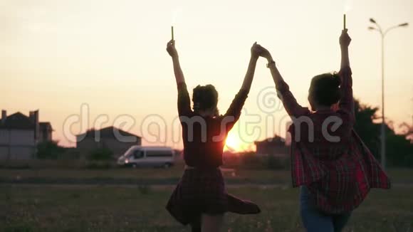 在日落时两个女朋友向前走并挥舞着烟火蜡烛镜头耀斑慢镜头视频的预览图