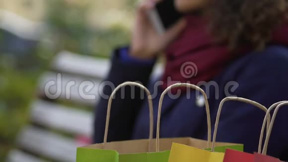 购物后坐在长椅上与朋友通电话的多种族女士视频的预览图