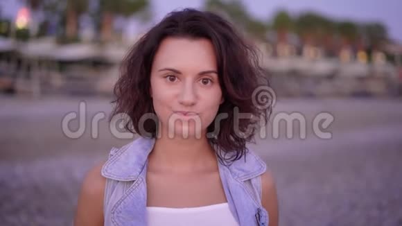 一位短发和卷发的年轻女子的肖像她穿着牛仔布夏天站在海滩上视频的预览图
