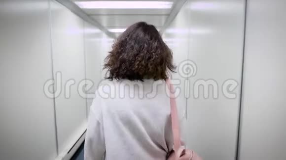 一位留着短发和卷发的女士沿着一条狭窄的走廊行走以便登上一架飞机她的背上是一个时尚的人视频的预览图