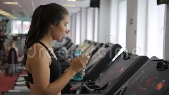 女运动员在跑步机上行走在室内运动俱乐部喝水视频的预览图