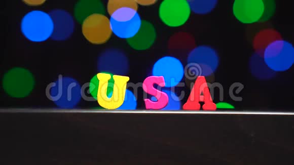 色彩缤纷的美国字由多种颜色的木制字母在抽象模糊的灯光前背景视频的预览图
