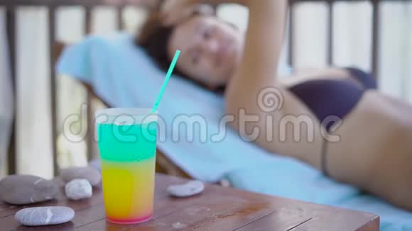 一个躺在吊床上穿着泳衣的女人用手伸到杯子里喝一杯一个女人靠在上面视频的预览图