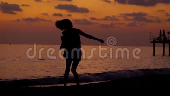 一个女人在日落的背景下移动的剪影一个女人在傍晚的沙滩上跳舞她的头发视频的预览图