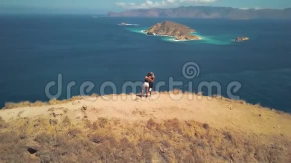 两个快乐的朋友站在山顶上眺望海湾拥抱和欣赏野生的美丽视频的预览图