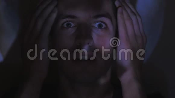 一个年轻人在电视或电脑显示器上看恐怖电影的肖像她脸上的倒影视频的预览图