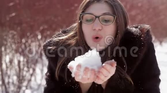 戴着眼镜和貂皮大衣的快乐女孩把手里的雪吹得通红视频的预览图