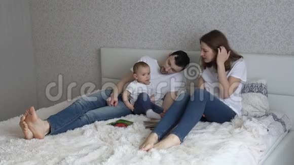 年轻的家庭在家里睡觉爸爸妈妈和他们的女儿一起玩视频的预览图