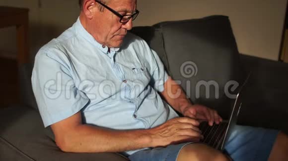 一位坐在家里的椅子上看电脑屏幕的手持笔记本电脑的老人的画像视频的预览图