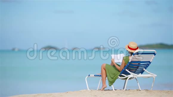 年轻女子在热带白海滩上读一本关于躺椅的书视频的预览图