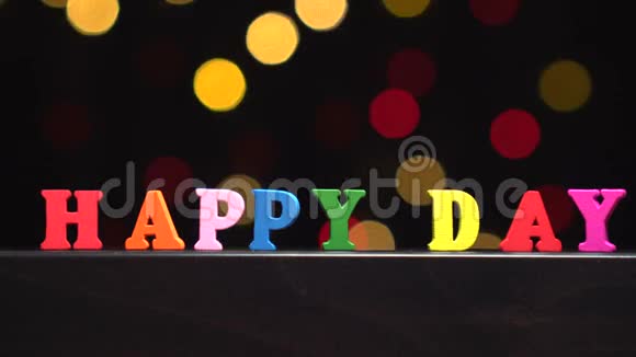 色彩斑斓的词语快乐的一天从抽象模糊的灯光前的多种颜色的木制字母背景视频的预览图
