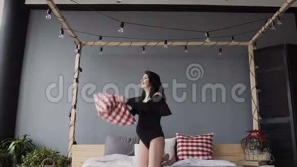 怀孕的黑发女孩高兴和扔枕头穿着黑色泳衣的女人视频的预览图