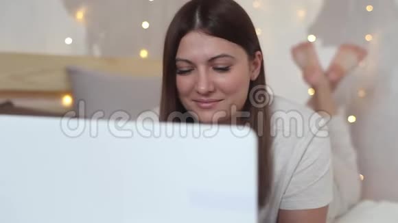 漂亮的女孩喜欢躺在床上的笔记本电脑视频的预览图