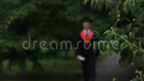 穿着学术服装的男学生在公园里快乐地散步和跳跃毕业视频的预览图