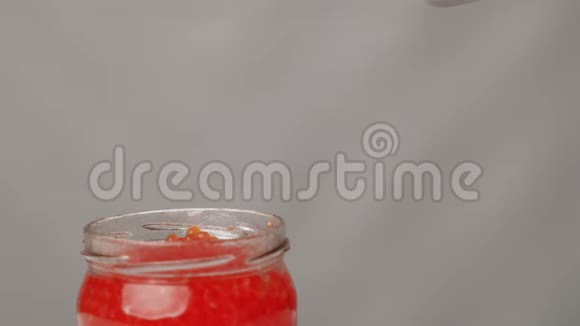 拍摄女用手从玻璃瓶中用勺子拿红鱼子酱视频的预览图