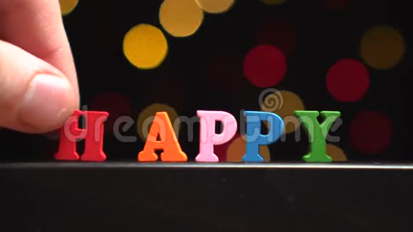 在抽象模糊的灯光前用多种颜色的木制字母书写快乐的视频的预览图