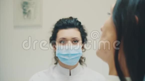 年轻的医生是一个穿着医用白色衣服和口罩的女人做一个病人的回顾在考试期间视频的预览图