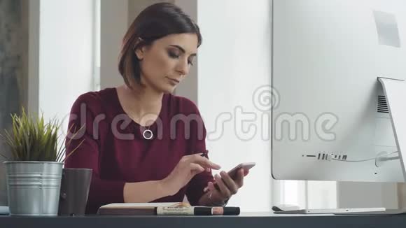 现代女性看着智能手机在笔记本上做笔记视频的预览图