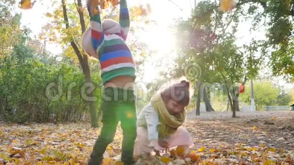 姐姐和哥哥在树的背景上把黄色的叶子扔到空中在背光下玩耍视频的预览图