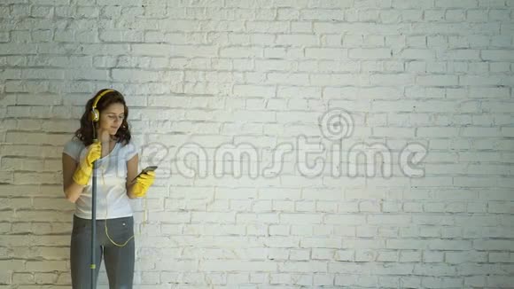 幸福的女人戴着耳机唱歌假装拖着麦克风在白色的砖墙里视频的预览图