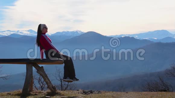 年轻女子坐在外面的长凳上看着有山的图画景观视频的预览图