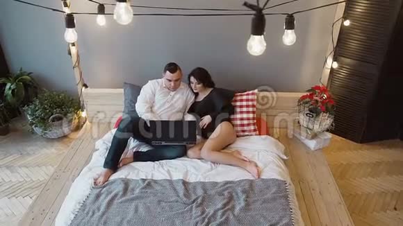 俯视图一个年轻男子和怀孕的妻子坐在床上在家里使用他们的笔记本电脑怀孕概念视频的预览图