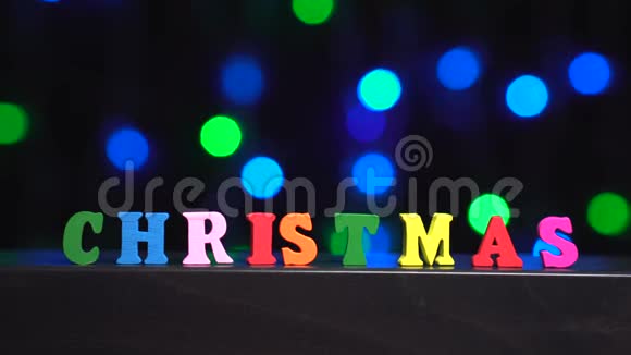 色彩斑斓的圣诞字由多种颜色的木制字母在抽象模糊的灯光前背景视频的预览图