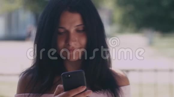 一位年轻女士在一个夏天的公园里看她的智能手机上的短信的肖像美丽的年轻姑娘黑发视频的预览图