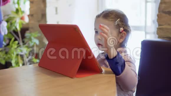 可爱的小女孩在平板电脑上看动画片在咖啡馆等妈妈视频的预览图