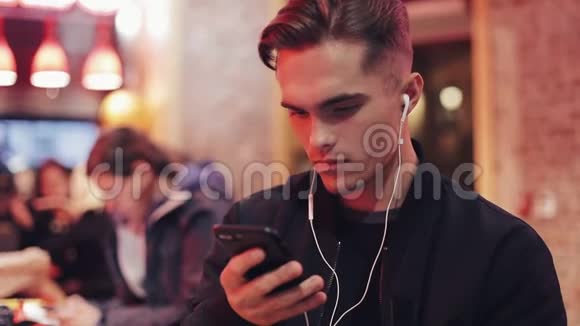 年轻人晚上在咖啡馆里听智能手机上的音乐视频的预览图