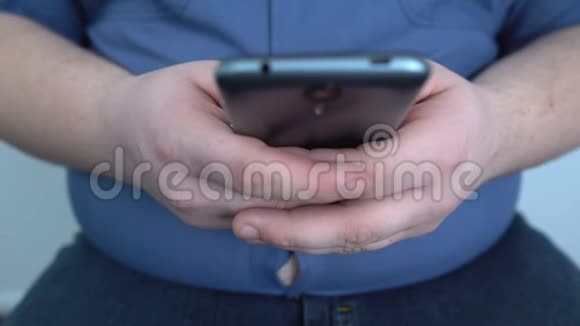 懒惰的胖子在智能手机里玩游戏聊天朋友久坐不动的生活方式视频的预览图
