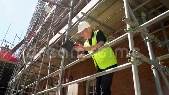 建筑工地上的建筑工人站在脚手架上在剪贴板上写字用手机说话视频的预览图