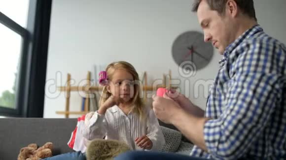可爱的父亲在他可爱的小女儿的头发上调整卷发视频的预览图