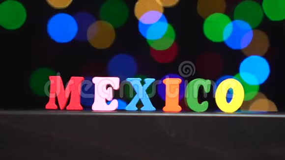 色彩斑斓的词墨西哥由多种颜色的木制字母在抽象模糊的灯光前背景视频的预览图