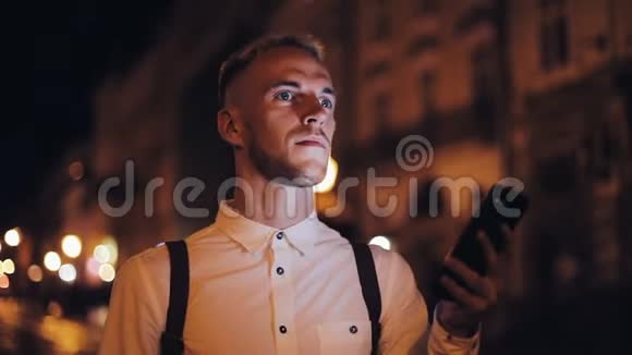 年轻迷人的男人用智能手机走在夜城的街道上交流旅游旅游约会商务视频的预览图