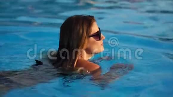 戴太阳镜的金发女人正在一个盆的蓝色水中游泳近距离视频的预览图