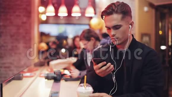 年轻人晚上在咖啡馆里听智能手机上的音乐视频的预览图