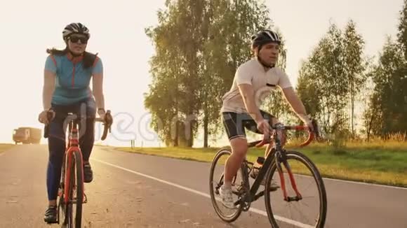 一对骑自行车的夫妇在日落时分骑着自行车走在公路上在高处玩耍视频的预览图