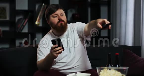 胖子看电视在他的智能手机里打字他点了家常菜营养不良食物的概念视频的预览图