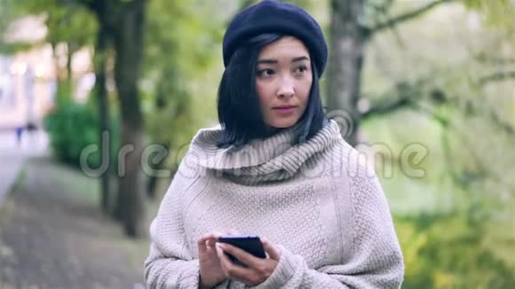 美丽的亚洲女人在秋天的公园里带着智能手机视频的预览图