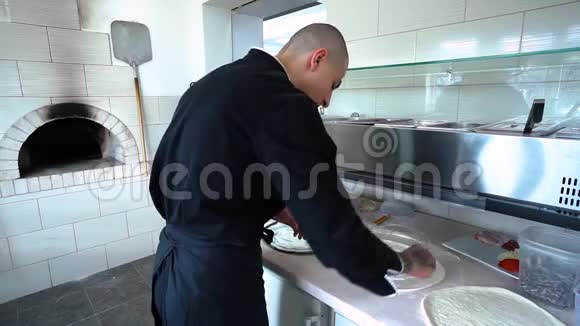 一个年轻的披萨师在餐厅的厨房准备披萨厨师把白酱涂在面团上视频的预览图