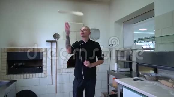 一个年轻的披萨师在餐厅的厨房准备披萨厨师把面团在空气中旋转并展开视频的预览图