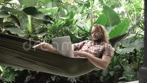 一个坐在吊床上手提电脑的人异国情调的背景视频的预览图