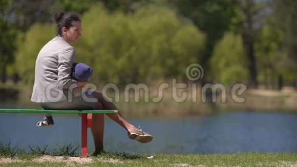 妈妈带着孩子坐在湖边的长凳上视频的预览图