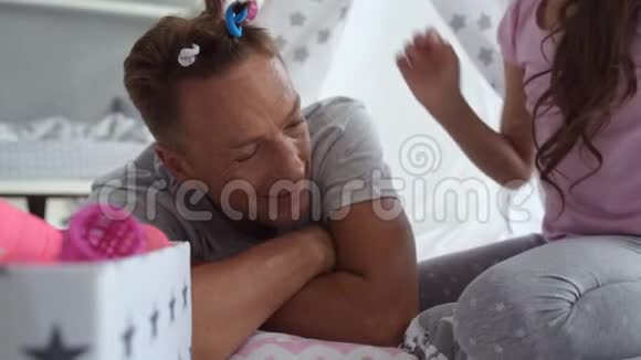 小漂亮的女孩把卷发贴在她父亲的头发上视频的预览图